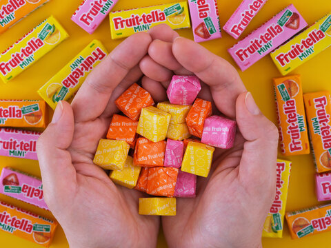 Tambov, Russian Federation - January 22, 2023 A woman holding a pile of different flavoured Fruit-tella candies over a background of fruitella mini packs.