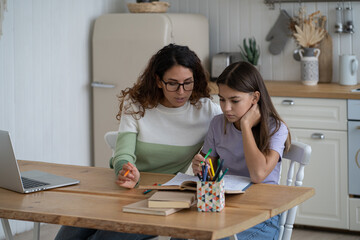 Young mother teaching teen girl daughter at home, mom helping sad frustrated kid with difficult school task, supporting child in remote learning. Woman freelancer balancing parenting and remote work