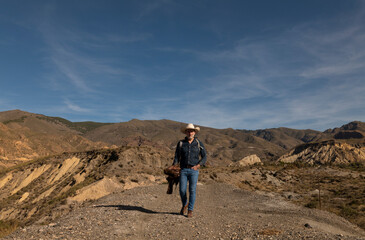 Fototapeta na wymiar Adult man in cowboy hat walking on dirt road in desert. Almeria, Spain