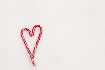 Festive minimalistic white background. A heart of sweet red striped candies on a background of white snow. Love. Valentine. Creative gift ideas for Valentine's Day. The 14th of February. Photo with a