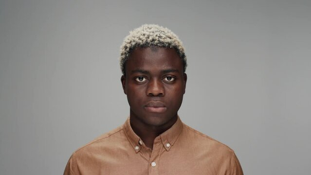 Portrait of Young Black Man Looking at Camera Alone in Color Studio Shot. Adult Afro Boy Isolated Alone on Grey Background Close up. African American Person in Trendy Clothes Opening Beautiful Eyes