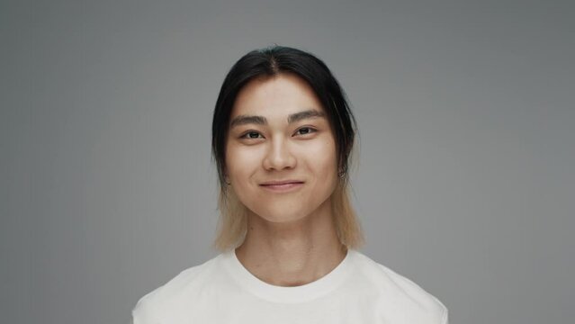 Portrait of Young Korean Man Looking at Camera in Color Studio Shot. Adult Japanese Boy Isolated Alone on Grey Background Closeup. Asian Person Opening Beautiful Eyes and Smiling Friendly and Happy