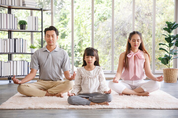 Young  asian family with daughter sit on floor practice yoga together, happy parents with girl child rest on floor meditate relieve negative emotions on weekend at home.