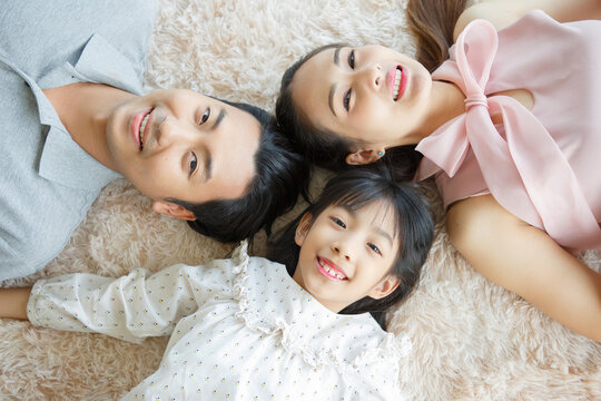 Portrait of a happy young family. Mom; dad and daughter look at the camera and smile. The faces of Asian parents and their child lay down on floor in living room. Family funning in living room.