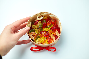 Woman hand with tasty jelly bears candy in present box on white background, flat lay candy gummy bear, top view, copy space.