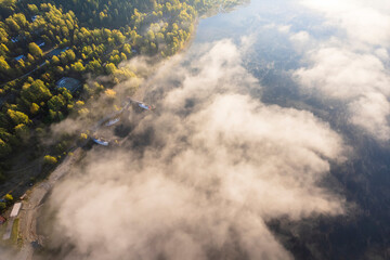 Clouds over lake and houses next to forest