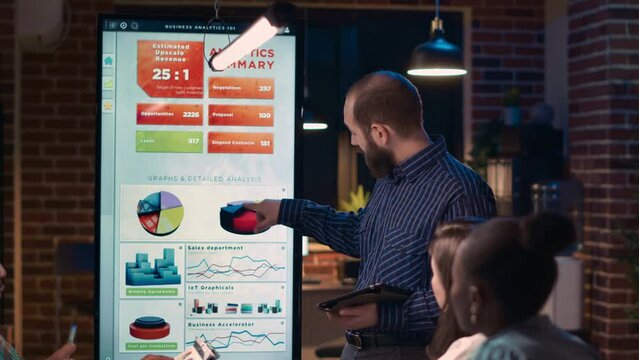 Company analyst explaining statistics diagrams, giving presentation in business meeting, holding digital tablet. Employee showing analytics research charts on screen at night time. Handheld shot. - Powered by Adobe