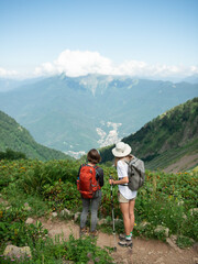 Fototapeta na wymiar Two women with backpacks and trekking poles hiking in mountains enjoying the view during sunny day