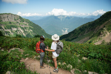 
Two women with backpacks and trekking poles hiking in mountains enjoying the view during sunny day - 566932895
