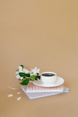 Cup of black coffee, books and a sprig of apple blossoms on a beige background with a copy space