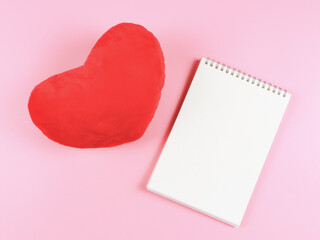  flat lay of opened  notebook with red heart shape pillow  on pink background with copy space. Love, Valentine's day, memory.