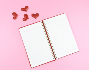 lat lay of opened red notebook or diary with red glitter hearts on pink background with copy space. Love, Valentine's day, memory.