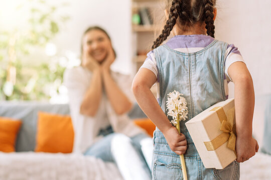 Child holding a gift and flowers behind her back in front of her mother. mother's day