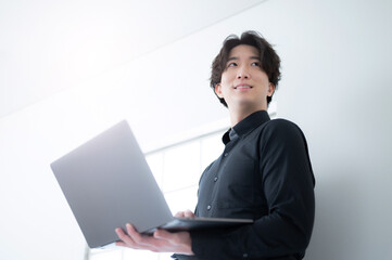 Handsome Asian man holding computer and looking up