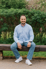 Obraz premium Attractive smiling man sitting alone on a park bench