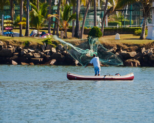 Fototapeta premium fisherman in his canoe using a net to fish in the middle of the sea