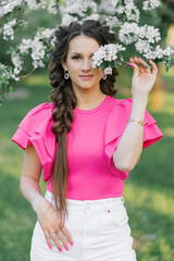 Happy to a young beautiful woman in a spring garden holding a branch of apple blossoms and smiling