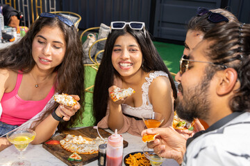 Group of cheerful indian friends girls and boy having fun eating pizza talking and laughing together at restaurant cafe. Summer season, food and drinks. Top view. Fast food.