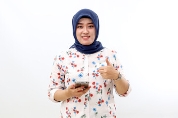 Happy asian muslim woman standing while holding a cell phone and showing thumbs up.