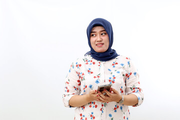 Happy asian muslim woman holding a cell phone while glancing sideways. Isolated on white background