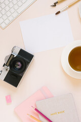The workspace of a blogger or photographer. Keyboard, camera, a blank sheet of paper and a pen for calligraphy, a cup of tea on a beige background