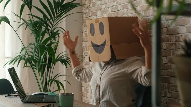 Overjoyed person working on laptop and wearing cardboard box carton on his head. Concept of success and identity online. Winner using computer. Joyful expression people in business technology activity