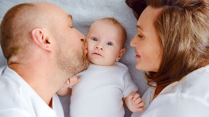 Happy family. Newborn baby with happy parents, top view. Healthy newborn baby in a white t-shirt with mom and dad. Close up Faces of the mother, father and infant baby. Cute Infant boy and parents