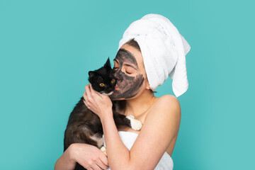 Woman with black cat apply charcoal facial mask mask isolated over blue studio background. Spa, cosmetic mask. Beautiful woman with black clay facial mud mask.