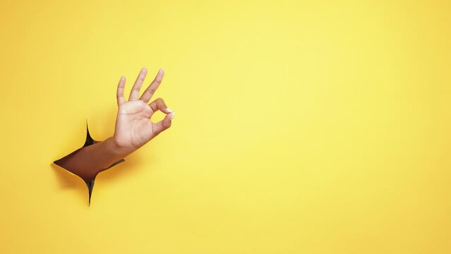 Okay gesture. Perfect choice. Approval satisfaction. Female hand showing ok yes sign in yellow breakthrough hole ripped paper wall advertising copy space background.