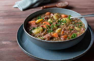 Lentil soup or stew. Cooked with vegetables, potatoes and pork meat isolated on wooden table. Closeup and front view