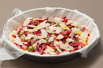 Fresh homemade Italian pizza with bacon, olives, capers and parmesan cheese ready for baking