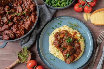 Italian pork ragout with creamy polenta and green beans on wooden table for dinner or lunch. Flat lay