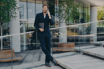 Full length shot of elegant businessman in formal clothes has telephone conversation