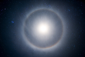 halo from the moon in the starry sky at night. A lunar halo around the Moon, showing several color bands in its iridescent form, in early winter. long exposure. - obrazy, fototapety, plakaty