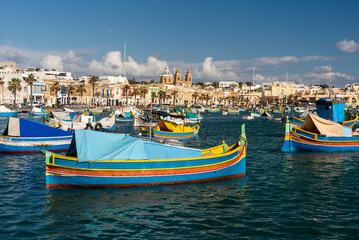 Fototapeta na wymiar Old Colorful Boats Luzzu in Marsaxlokk harbor at sunny day. Blue sky with clouds