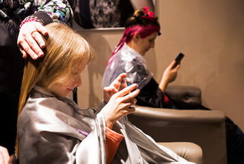 little girl with long white hair on a haircut plays in a gadget when the hairdresser cuts her hair