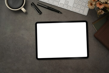 Top view of digital tablet with blank screen, cup of coffee and notepad on black slate texture background