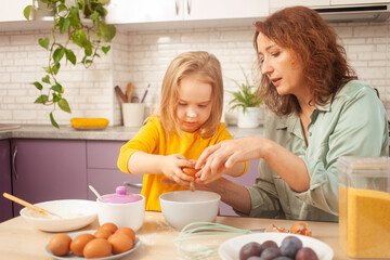 Grandmother and granddaughter prepare cake dough, spend time together, family relationships, love. add an egg to the dough