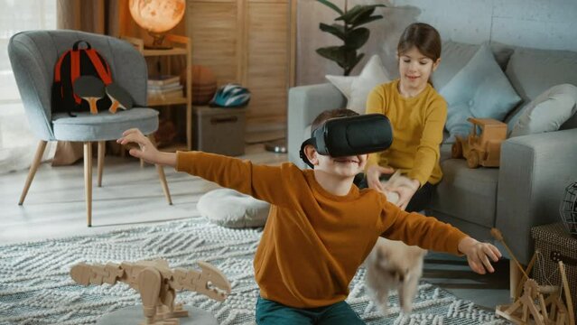 Boy uses VR glasses to play a virtual game while his sister plays with a dog in the room