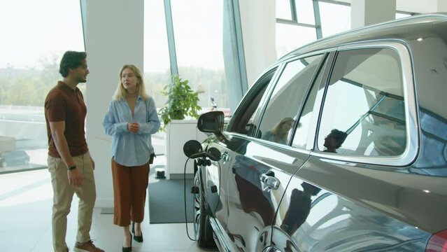 Young married couple looking at crossover car in dealership showroom and discussing its design