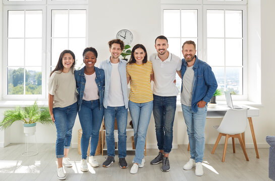 Group Portrait Of Happy Multiracial Friends. Team Of Cheerful Joyful Beautiful Young Diverse People In Casual Clothes Standing Together, Hugging Each Other, Looking At Camera And Smiling