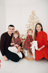 Christmas family photo of dad, mom and two daughters in a red dress sitting on a rocking horse. Christmas photo near the tree. family red Christmas clothes