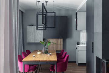 Elegant dining room interior design with velvet chairs, design wooden table, lamps and beautiful personal accessories. Open space. Concrete walls. Modern home decor. Template.