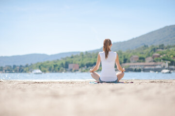 Fototapeta na wymiar Frau am Seeufer Sandstrand beim Meditieren in Italien am Lago Maggiore
