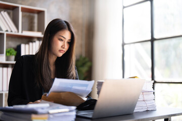 Young Asian businesswoman working on laptop computer, stressed has a headache and thinks hard from work at the office.