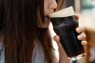 Asian lady holding the glass with one hand and sipping the foam of the nitro cold brew coffee