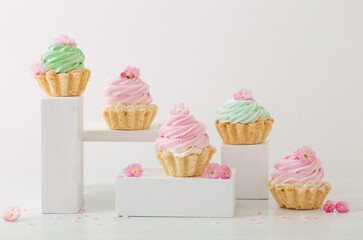 pink and green cupcakes with spring flowers  on wooden podiums on white  background