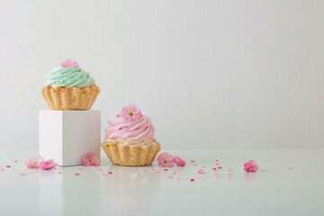 pink and green cupcakes with spring flowers  on wooden podiums on white  background