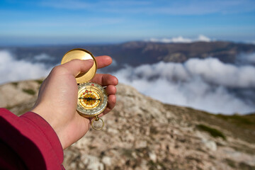 Closeup hand holding compass with mountain and clouds background. Closeup of man tourist hand...