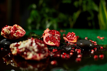 Piece of  pomegranate and whole fruits on black and green  background with juice drops, space for...
